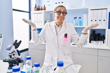 Young woman working at scientist laboratory shouting and screaming loud to side with hand on mouth. communication concept.