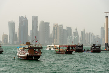 Traditional dhow pearl fishing boat at The Corniche with skyscrapers misty view in the background , Doha, Qatar - obrazy, fototapety, plakaty