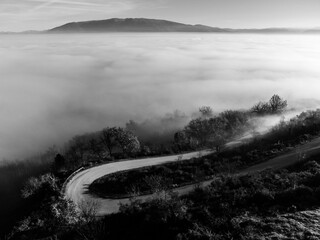 Aerial drone view of a curcy road above a sea of fog - 614541083