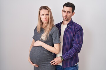Fototapeta premium Young couple expecting a baby standing over white background skeptic and nervous, frowning upset because of problem. negative person.