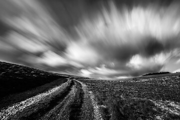 Spectacular long exposure view of clouds above a path on a hill - 614542263