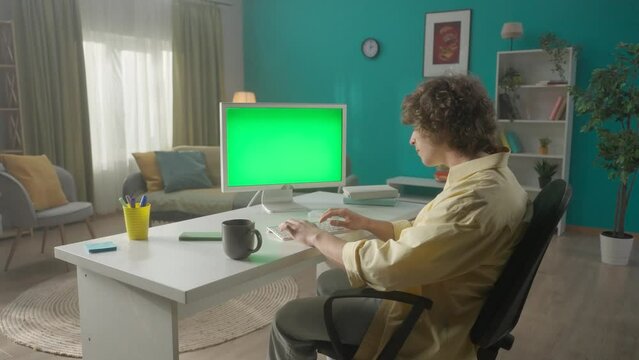 A young man drinks morning coffee and works at a computer with a green screen. Green screen computer monitor close up. The concept of technology, connection, communication. HDR BT2020 HLG Material.
