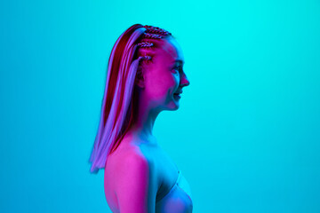 Profile portrait of young pretty girl with cute hairstyle posing, looking straight against blue studio background in neon light. Concept of youth, emotions, beauty, lifestyle, ad