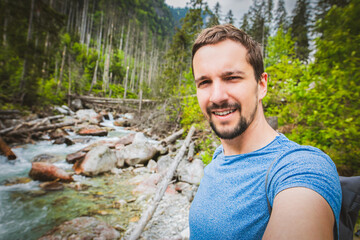 A selfie of a happy guy on a trail, with a mountain stream in the background