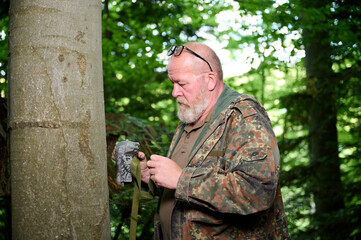 Hunter sets a trail camera on a tree in the forest. Trail cameras are often used by hunters for automatic photography or video shooting of wildlife in the forest.