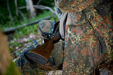 Crop view of the hunter sitting on the log in the forest. Hunter man in camouflage suit in the...