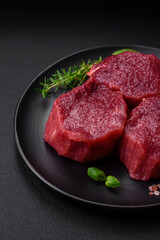 Juicy raw beef with spices, salt and herbs on a dark concrete background