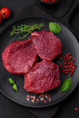 Juicy raw beef with spices, salt and herbs on a dark concrete background