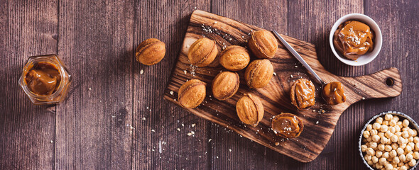 Fresh nut shaped cookies filled with boiled condensed milk on a board top view web banner