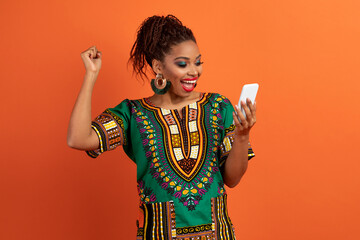 Emotional young african lady using cell phone, orange background