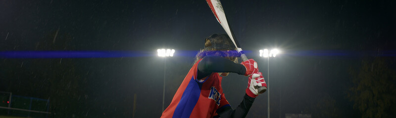 Portrait of Caucasian kid boy baseball player practicing hits alone on a rainy evening. Shot with...