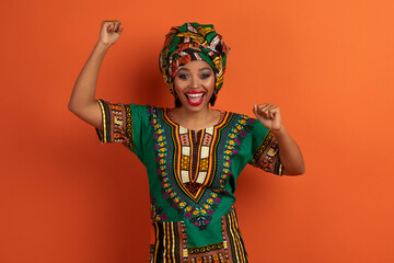 Super happy young african lady celebrating success win on orange