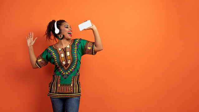 Happy black woman in african clothing singing, dancing on orange