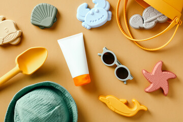 Flat lay silicone beach toys, sunglasses, hat, sunscreen lotion tube for babies on sand color background.