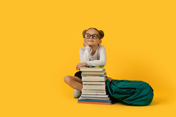 Cute Elementary School Girl Sitting At Books Stack Over Yelow Background