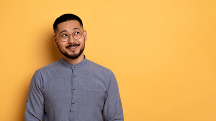 Pensive Young Asian Man Looking Aside At Copy Space And Smiling