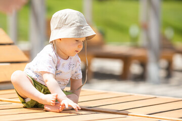 Cute baby boy is sitting on wooden beach chair near the sea during family vacation