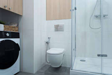 White bathroom with bath shower, toilet, wooden cabinet and washing machine. Stylish interior of washroom with wc.