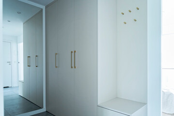 Luxurious corridor with mirror, white wall and wardrobe. Door handles and hanger in hallway in new apartment. Interior of design architecture.