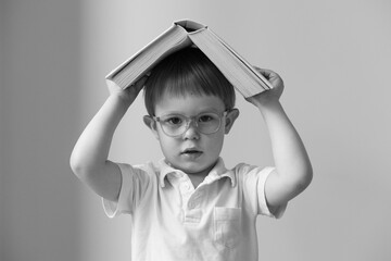 little boy with glasses holding a book above his head, black and white shot