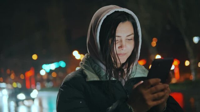 Young pretty woman text messaging on her smart phone in city street at night