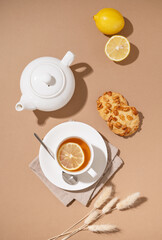Creative layout of a cup of herbal tea with cookies, lemon and teapot on a brown background with a shadow. Healthy drink concept.