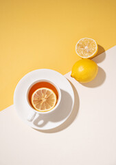 A cup of tea with lemon on a white and yellow background with a shadow. Healthy and detox drink concept.