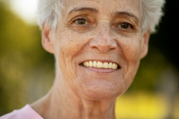 Portrait of smiling elderly woman at park. Happy thoughful mature woman relaxing outdoor.