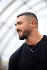 Fototapeta premium Hombre musculado con camiseta negra sonriendo mientras ve algo que le hace feliz. Concepto de emociones y sensaciones.