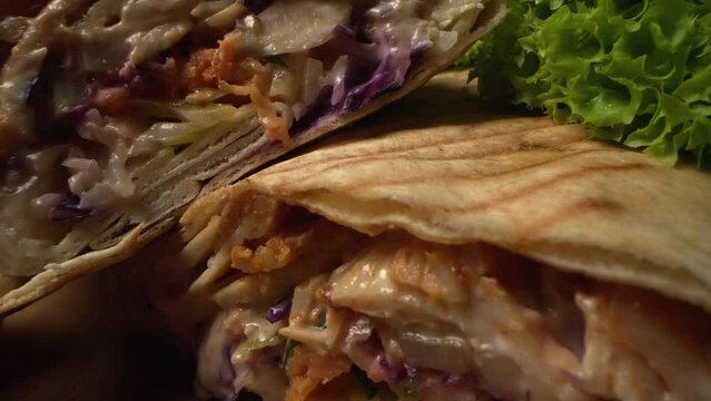 Tasty doner kebab close up on wooden background. Tortilla wrap with fried chicken meat and vegetables in macro. 4K ProRes