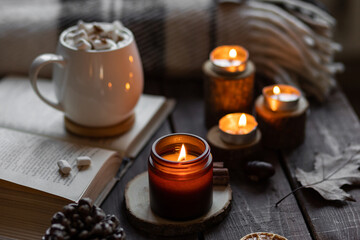 Obraz na płótnie Canvas Aromatherapy on a grey fall morning, atmosphere of cosiness and relax. Autumn cozy home composition with hot chocolate with marshmallow and candles. Wooden background, books, close up.