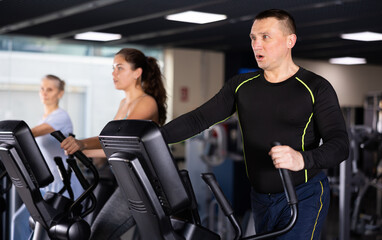 Fototapeta na wymiar Focused athletic man warming up on elliptical machine before strength training in modern gym..