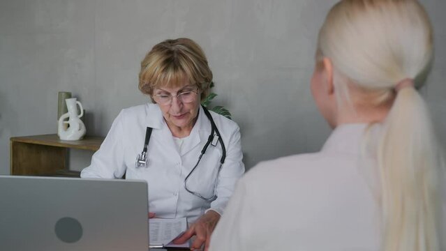 A positive elderly woman general practitioner doctor with a smile communicates with a female patient in her office and announces excellent good examination results. High quality 4k footage
