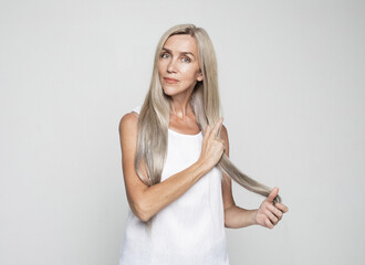 Beauty and old people concept: beautiful elderly woman touch long lovely grey hair over light grey background.