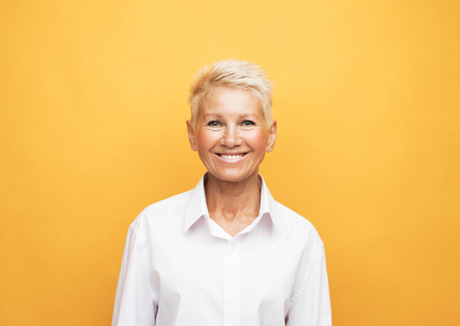 Elderly beautiful woman with a short pixie haircut on a yellow color background