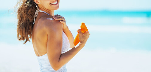 Smiling young woman on beach applying sun block creme