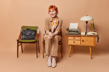Retro redhead smiling woman dressed in elegant costume prepares herself for job interview using old...