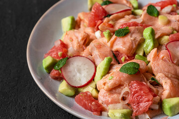 Chilean salmon seviche with grapefruit, avocado, radish, onion and mint in a plate with fork on black background. close up