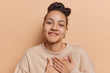 Photo of pleased Latin woman tenderly places her hands on heart conveying profound sense of...