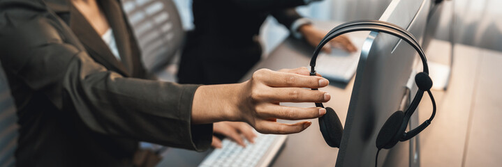 Panorama focus hand holding headset on call center workspace desk with blur background of operator team or telesales representative engaging in providing client with customer support service. Prodigy - obrazy, fototapety, plakaty