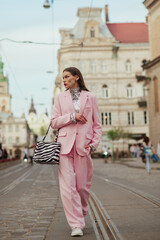 Fashionable elegant confident woman wearing trendy pink suit blazer, wide leg trousers, holding...