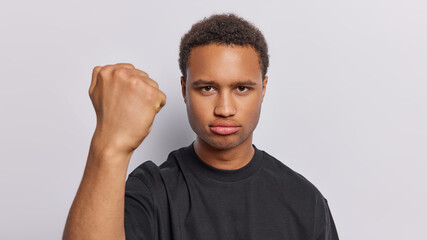 Angry dark skinned adult man clenches fist expresses negative emotions demonstrates his irritation dressed in casual black t shirt isolated over white background. People and annoyance concept