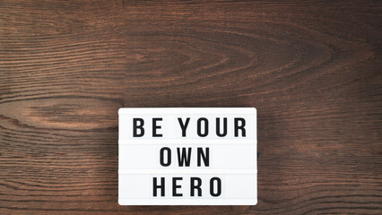 Be your own hero word on a letter board. Motivational quote concept. Motivational words on a white letter board on wooden table. High angle view