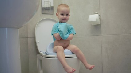 child toddler baby sitting toilet lavatory seat smiling looking camera hygiene education kid pee potty seat. concept healthy children. little child boy wc closet poop. caucasian baby blue shirt sit - Powered by Adobe