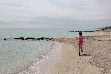 A girl in pink clothes runs along the seashore, childhood, the joy of life
