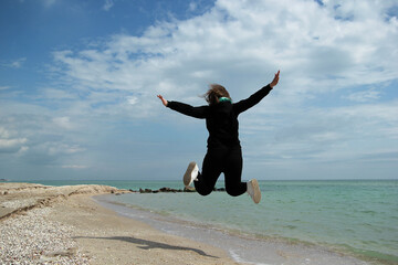 A girl enjoys life at sea, a girl in a black suit is jumping on a sunny paradise beach