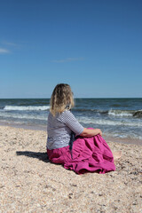 A woman sits on the seashore in a striped t-shirt and pink skirt, romance on the sea