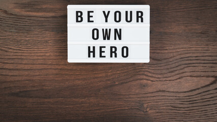 Be your own hero word on a letter board. Motivational quote concept. Motivational words on a white letter board on wooden table. High angle view