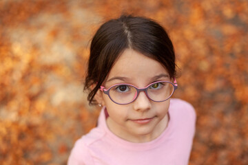 Portrait of a beautiful little girl with glasses in the autumn park