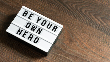 Be your own hero word on a letter board. Motivational quote concept. Motivational words on a white letter board on wooden table. High angle view